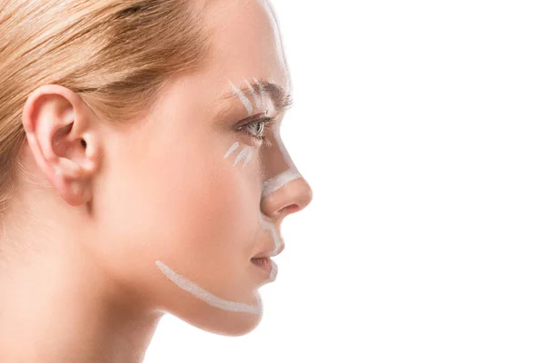 Vista lateral de la hermosa mujer con líneas blancas en la cara mirando hacia otro lado aislado en blanco, arte corporal - foto de stock