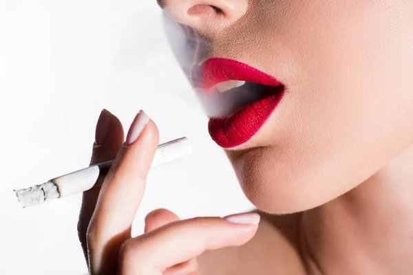 Imagen recortada de la mujer fumando cigarrillo y exhalando humo aislado en blanco - foto de stock