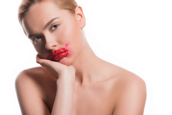 Mujer triste con lápiz labial rojo manchado en la cara mirando a la cámara aislada en blanco - foto de stock