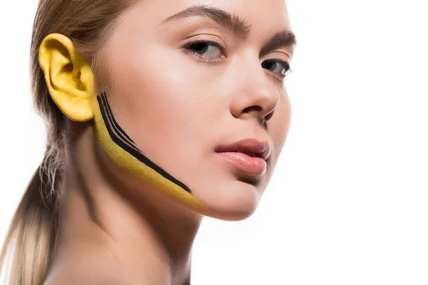Bela mulher com tintas amarelas e pretas na orelha e rosto isolado em branco — Fotografia de Stock