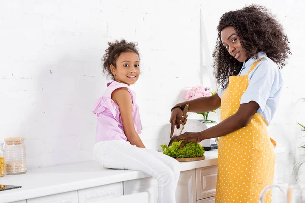 Hombre afroamericano y su hija cortar lechuga en la cocina - foto de stock