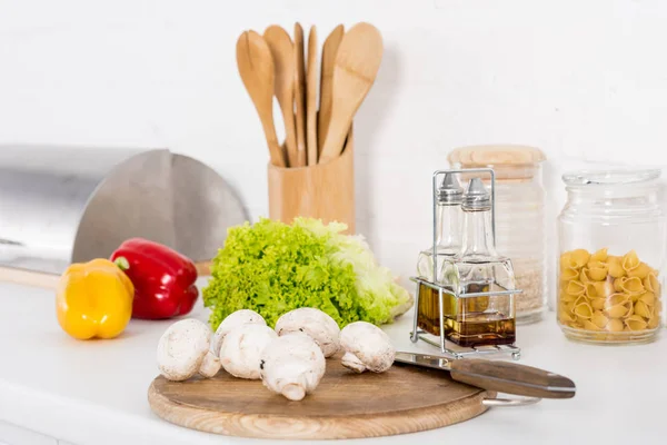 Bell peppers, lettuce and mushrooms on wooden board and oil in kitchen — Stock Photo