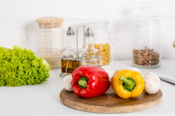 Перец, грибы и салат на деревянной доске на кухне с банками — стоковое фото