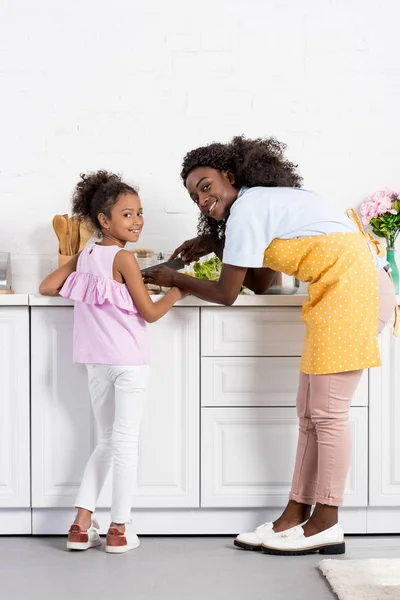 Африканская американская мать и дочь режут овощи на кухне — стоковое фото