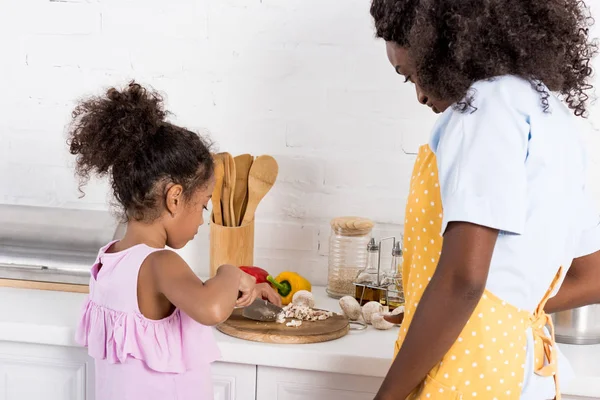 Africano americano mamá y hija cortar verduras en cocina - foto de stock