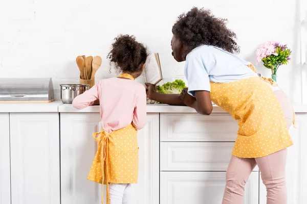 Visão traseira da mãe americana africana e filha lendo livro de receitas na cozinha — Fotografia de Stock