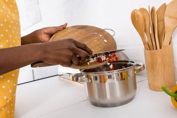Partial view of african american woman putting ingredientes into saucepan on kitchen — Stock Photo