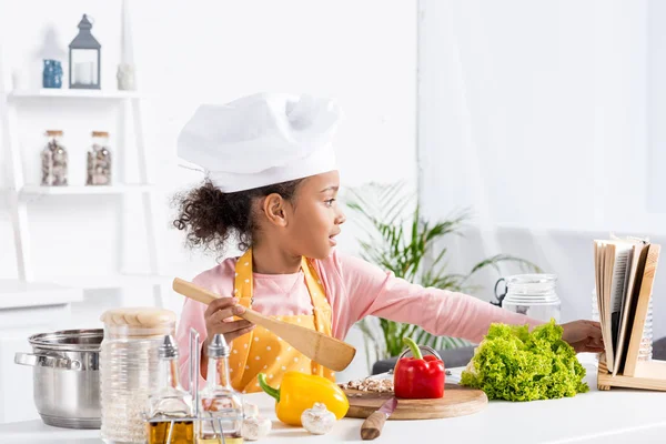 Adorable afroamericano niño en delantal y chef sombrero cocina en la cocina - foto de stock