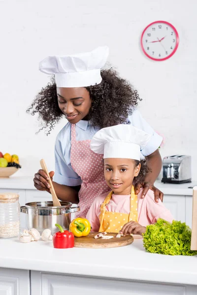 Africano americano madre e hija en chef sombreros cocinar juntos en cocina - foto de stock
