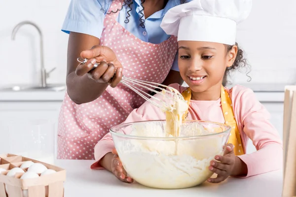 African american mother and daughter in chef hat making dough on kitchen — Stock Photo