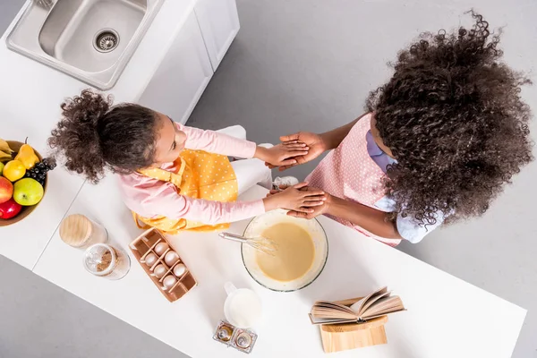 Overhead view of african american mother and daughter holding hands while making dough on kitchen — Stock Photo