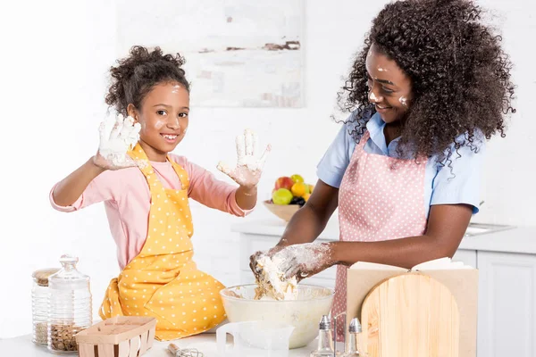 Souriant afro-américaine mère et fille pétrissant pâte dans un bol sur la cuisine — Photo de stock