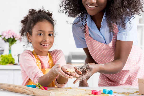 African american mother and smiling daughter making cookies from raw dough on kitchen — Stock Photo