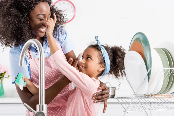 Afroamericano madre e figlia divertirsi mentre lavare i piatti insieme — Foto stock