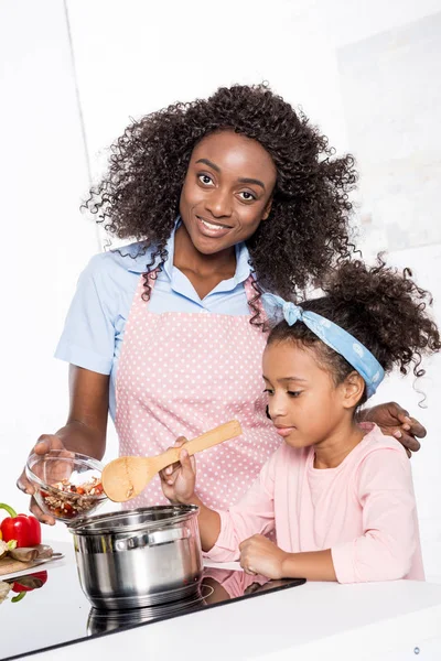 Afro-américaine mère et fille cuisine sur cuisinière électrique dans la cuisine — Photo de stock