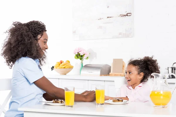 Африканская американская мать и дочь едят блины и апельсиновый сок на завтрак в столовой — стоковое фото