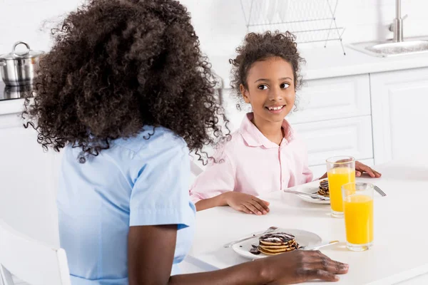 Familia afroamericana feliz teniendo panqueques y zumo de naranja para el desayuno en el comedor - foto de stock