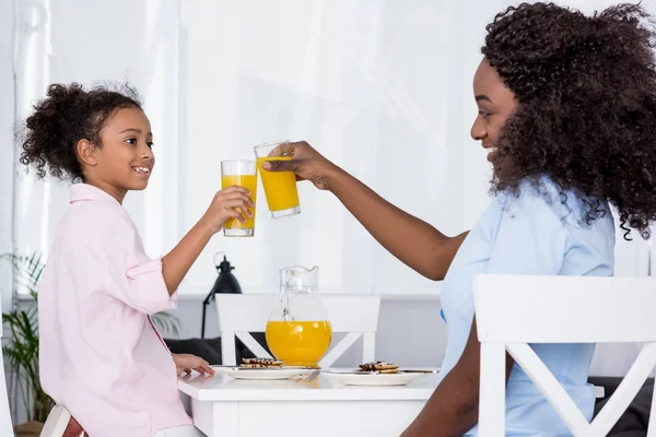 Felice afro-americano mamma e figlia bicchieri di clinking con succo d'arancia — Foto stock