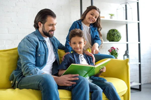 Feliz padre con dos lindos niños leyendo libro juntos en casa - foto de stock