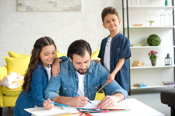 Niedliche glückliche Kinder schauen Vater Zeichnung mit Buntstiften zu Hause — Stockfoto