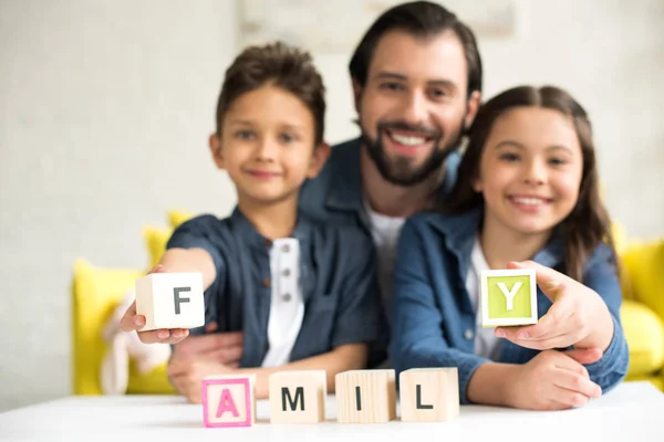 Heureux père avec deux adorables enfants tenant des cubes avec mot famille et souriant à la caméra — Photo de stock