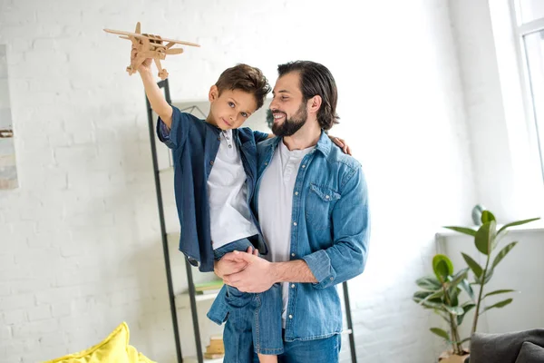 Glücklicher Vater mit niedlichem kleinen Sohn, der mit Spielzeugflugzeug spielt und in die Kamera schaut — Stockfoto