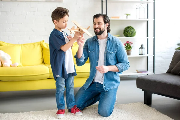 Padre felice e carino piccolo figlio che gioca con aereo giocattolo in legno a casa — Foto stock