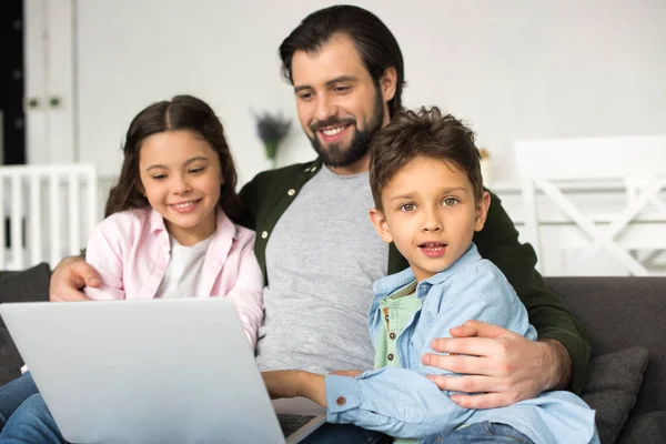 Smiling father with two adorable kids using laptop together at home — Stock Photo