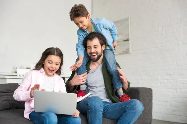 Happy father with two cute kids sitting on sofa and using laptop together — Stock Photo