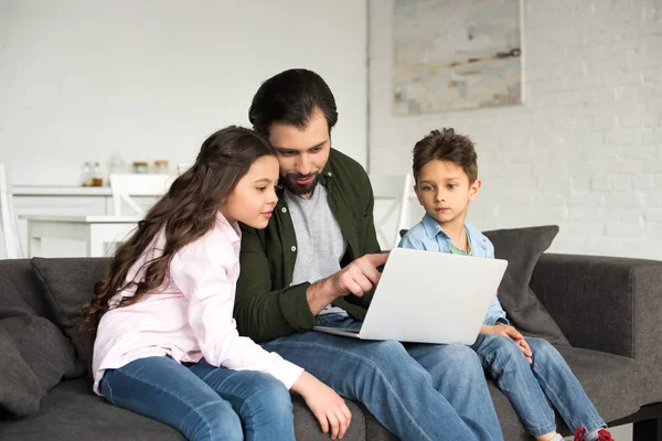 Father with two cute children sitting on sofa and using laptop together — Stock Photo