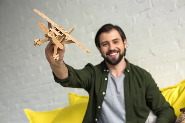 Vista de cerca del joven feliz jugando con el avión de juguete de madera y sonriendo a la cámara - foto de stock