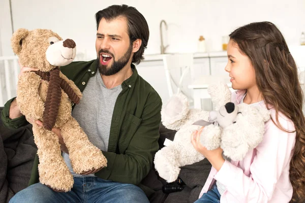 Feliz padre y linda hijita jugando con osos de peluche en casa - foto de stock