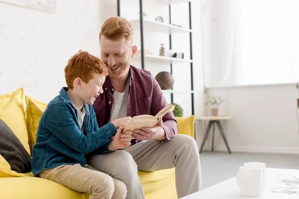 Happy father looking at cute smiling son reading book at home — Stock Photo
