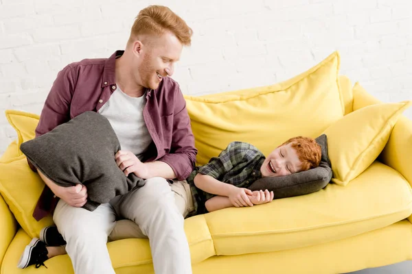Feliz padre e hijo divirtiéndose con almohadas en casa - foto de stock