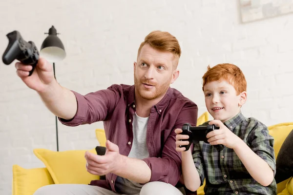 Sorridente rossa padre e figlio guardando lontano mentre si gioca con i joystick a casa — Foto stock