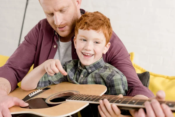 Plan recadré de père enseignant fils heureux jouer de la guitare à la maison — Photo de stock