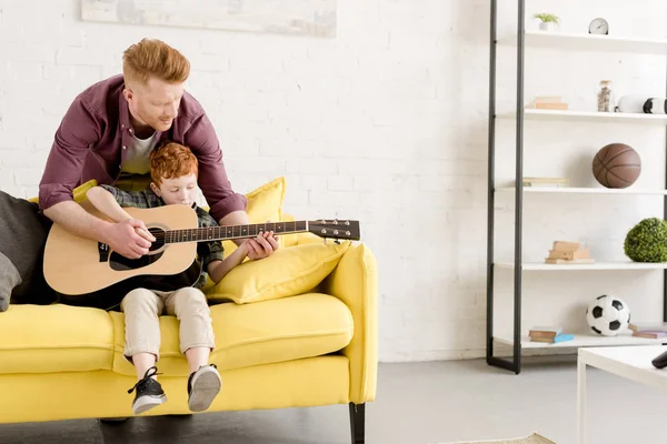 Padre enseñando lindo hijo pequeño tocando la guitarra en casa - foto de stock