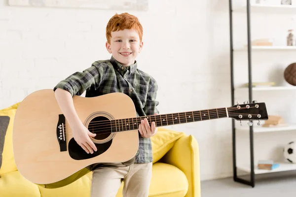 Menino bonito segurando guitarra acústica e sorrindo para a câmera — Fotografia de Stock
