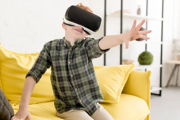 Adorable niño sonriente usando auriculares de realidad virtual en casa - foto de stock