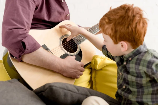 Обрезанный снимок милого мальчика, смотрящего на отца, играющего на гитаре — стоковое фото