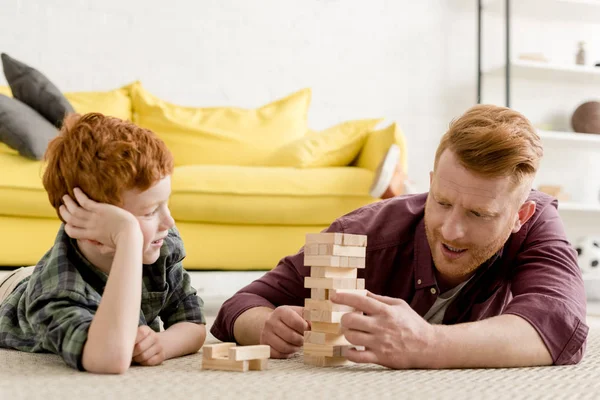Счастливые рыжие отец и сын играют дома с деревянными блоками — стоковое фото