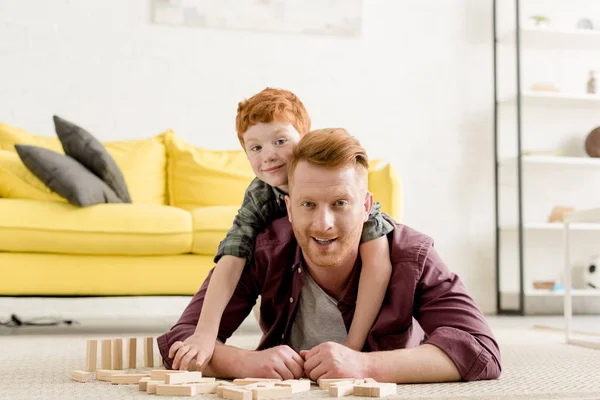 Glücklicher Vater und Sohn lächeln in die Kamera, während sie zu Hause mit Holzklötzen spielen — Stockfoto