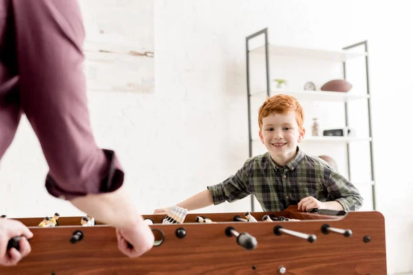 Recortado tiro de padre y lindo sonriente hijo jugando futbolín juntos en casa - foto de stock