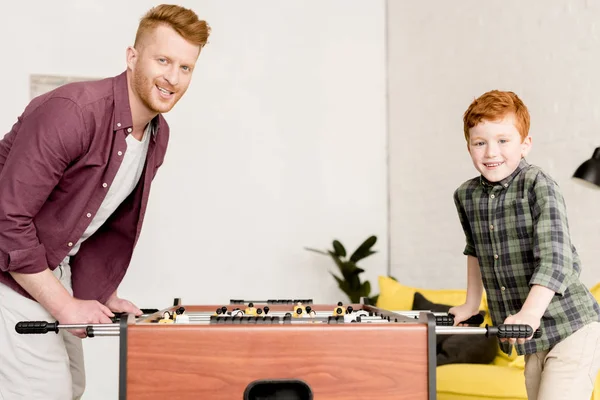 Glücklicher Vater und Sohn lächeln in die Kamera, während sie zu Hause gemeinsam Tischkicker spielen — Stockfoto