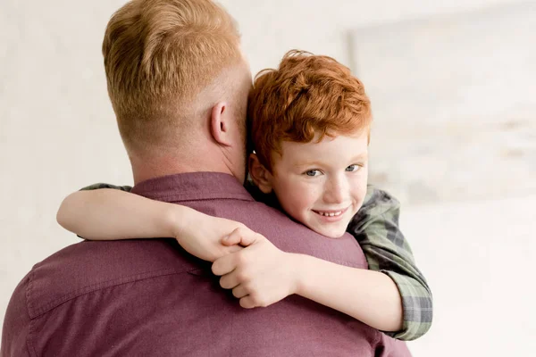 Lindo niño abrazando padre y sonriendo a la cámara - foto de stock