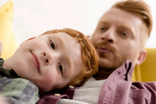 Close-up vista do menino bonito sorrindo para a câmera enquanto passa o tempo com o pai em casa — Fotografia de Stock