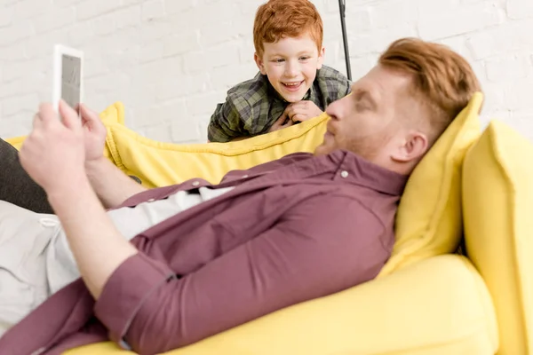 Niedliche glückliche kleine Junge sieht Vater mit digitalem Tablet zu Hause — Stockfoto