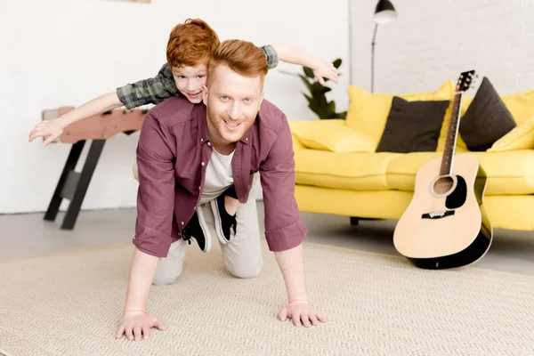 Heureux rousse père et fils souriant à la caméra tout en s'amusant ensemble à la maison — Photo de stock