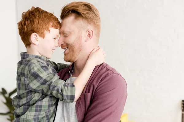 Side view of happy red haired father and son hugging at home — Stock Photo