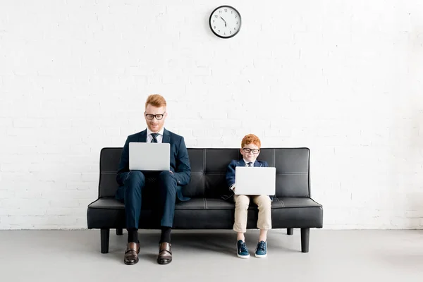 Padre sorridente e piccoli uomini d'affari figlio indossando occhiali e utilizzando computer portatili — Foto stock